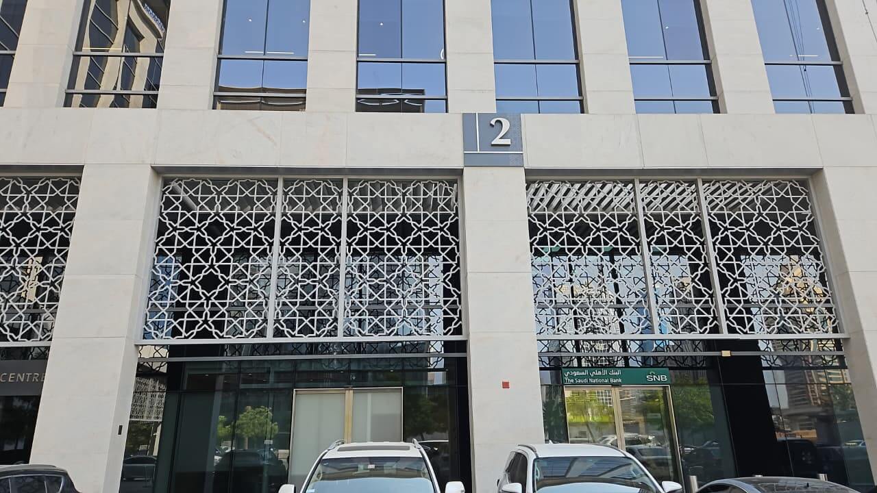Facade of a modern building featuring decorative metal lattice work on windows, with the number '2' prominently displayed. Several cars parked in front.