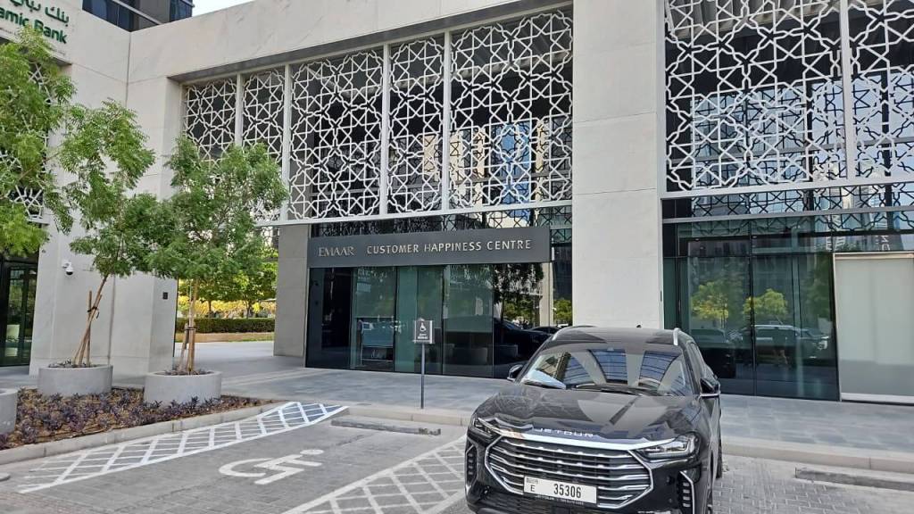 Exterior view of Emaar Customer Happiness Centre with decorative facade, surrounding greenery, and a parked black car in the foreground.