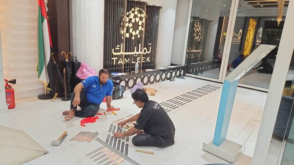 Two workers are assembling materials on the floor of a commercial space featuring the Tamleek logo, with a UAE flag in the background.