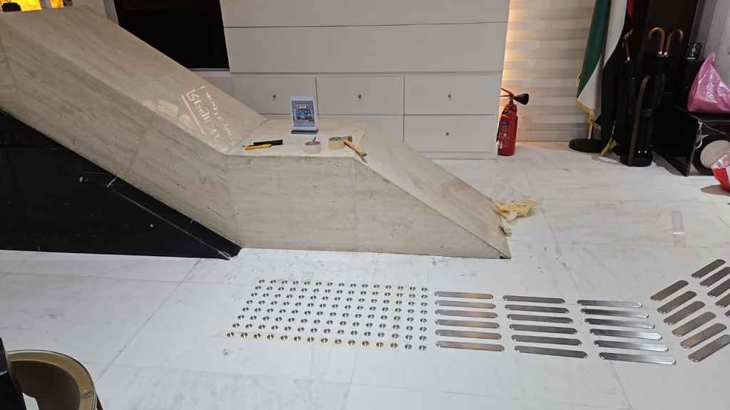 Interior view of a modern space featuring a sloped marble ramp and various construction tools. The floor has metal strips and a fire extinguisher in the background.