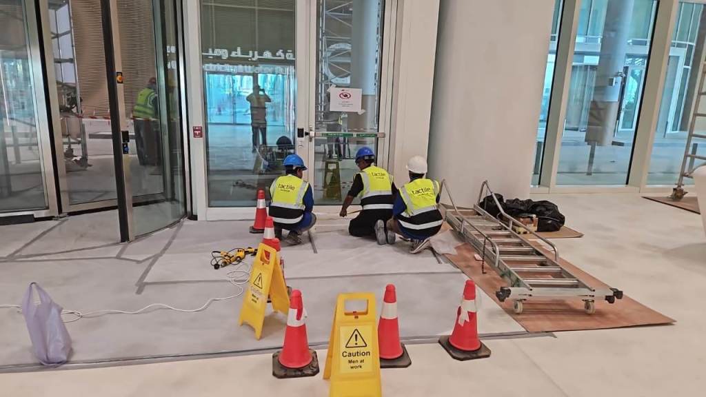 Construction workers in safety vests working on a building entrance with caution signs and traffic cones around.