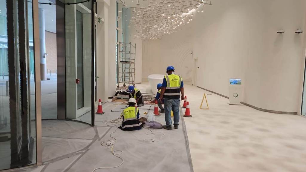 Construction workers installing materials in a modern building interior with a polished floor and a sophisticated lighting fixture.