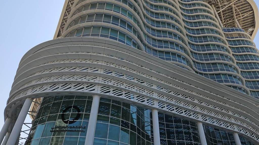 A modern building with a curved façade featuring large glass windows and an intricate white lattice design at the base.