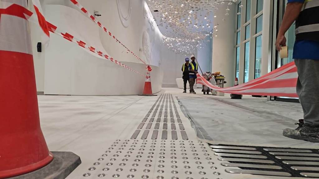 Construction workers setting up barriers and safety tape in a partially completed hallway with decorative lighting.