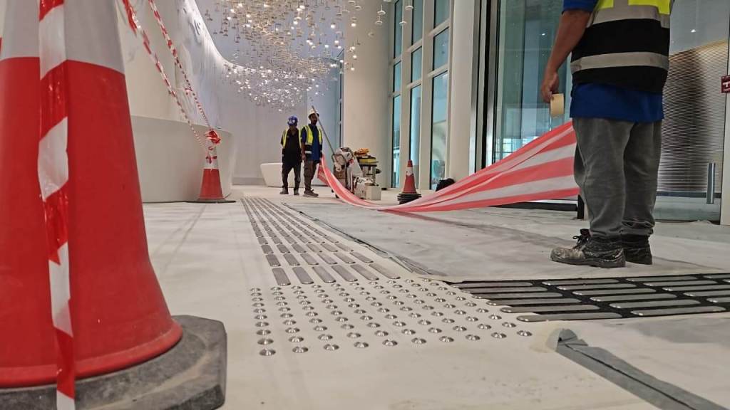 Construction site with workers laying striped caution tape on the floor, featuring traffic cones and a modern, well-lit interior.