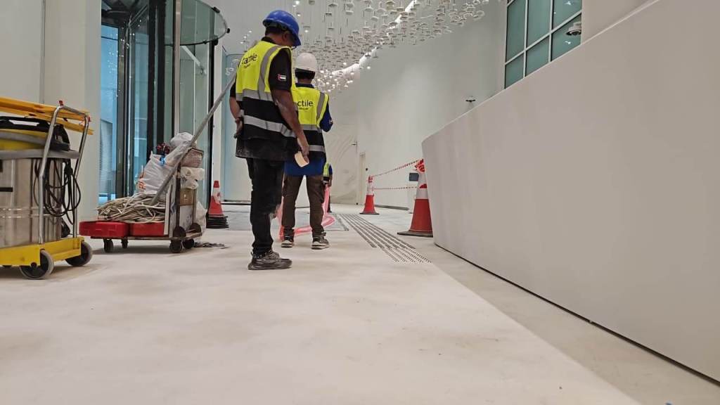 Construction workers in safety vests and helmets walking through a partially finished building interior with construction equipment nearby.