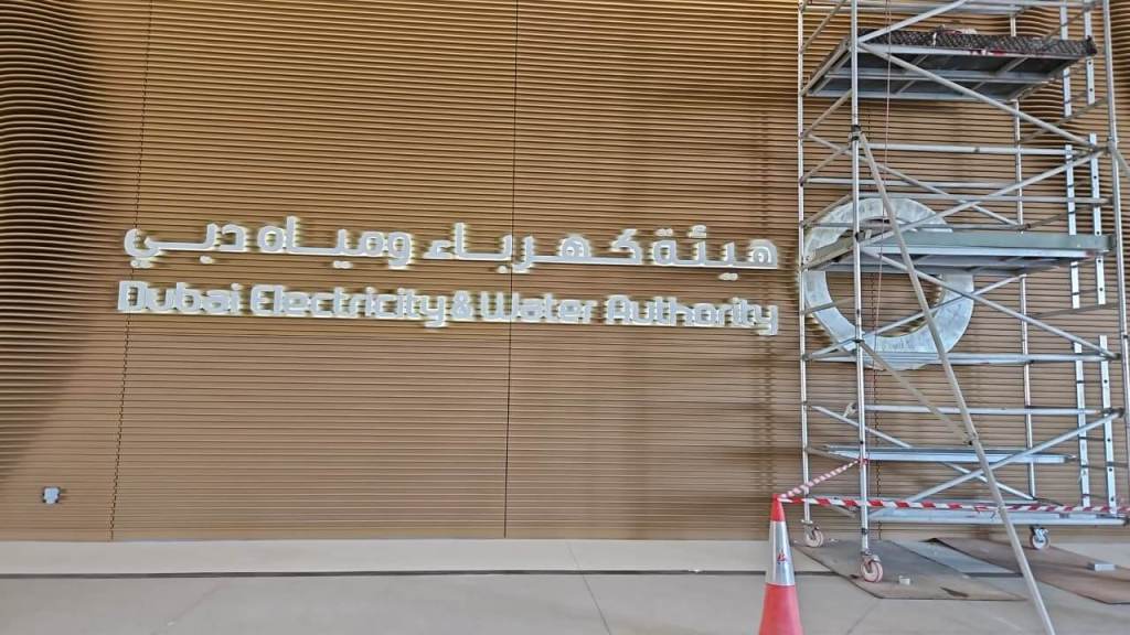 Interior wall display featuring the logo and name of Dubai Electricity and Water Authority in both Arabic and English, accompanied by scaffolding for installation.