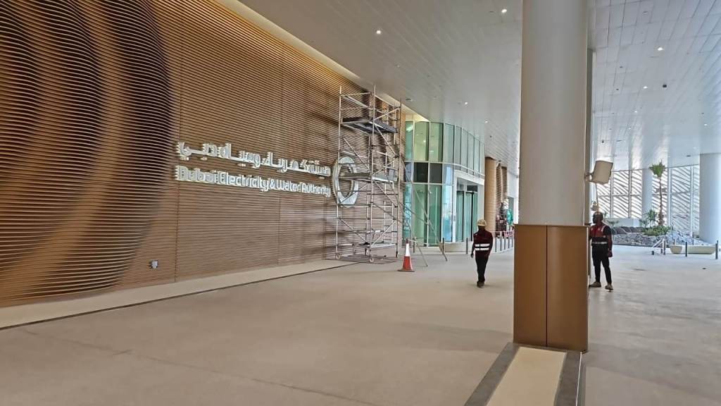 Entrance of the Dubai Electricity and Water Authority building, featuring a modern wooden wall design, scaffolding, and workers in red uniforms.