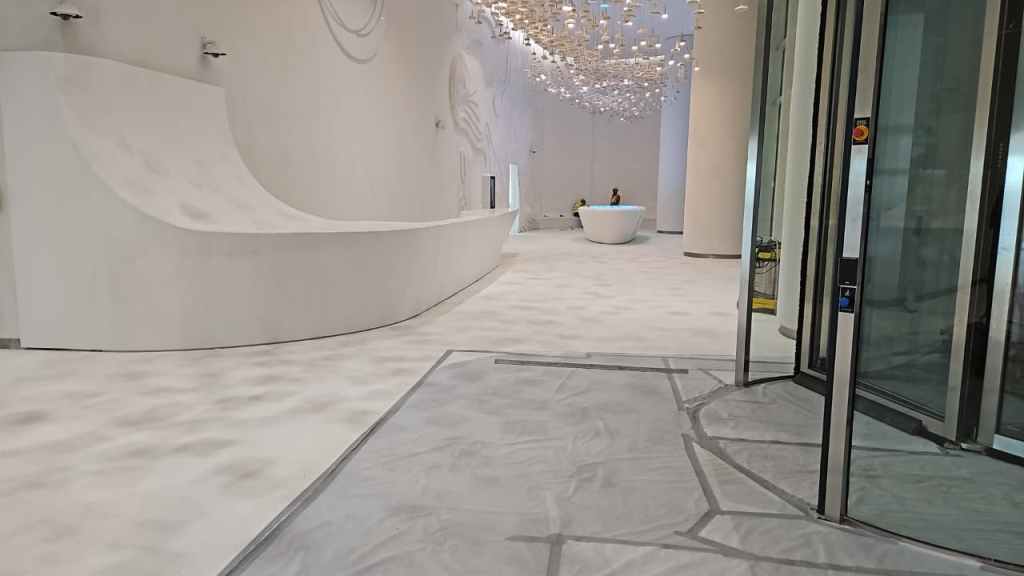 Interior view of a modern, spacious lobby featuring a curved reception desk, white walls, and a decorative ceiling. Soft lighting is present, along with a large, round seating area.