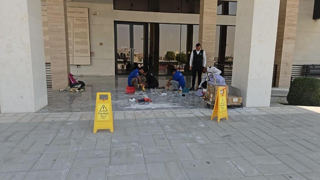 Construction workers performing maintenance outside a building with caution signs indicating wet floor.