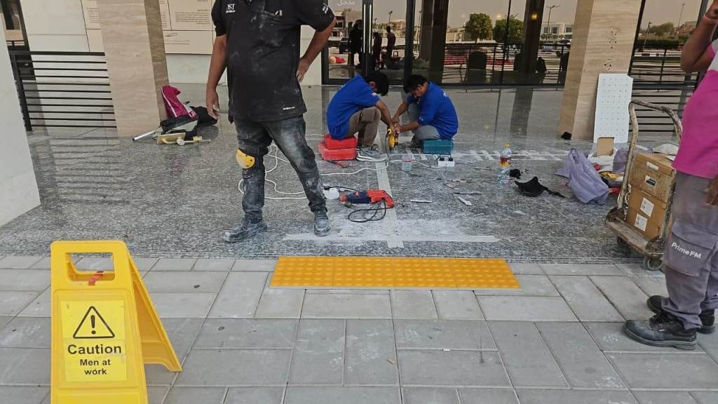 Construction workers doing renovations at an entrance with caution sign, tools, and materials scattered on the floor.