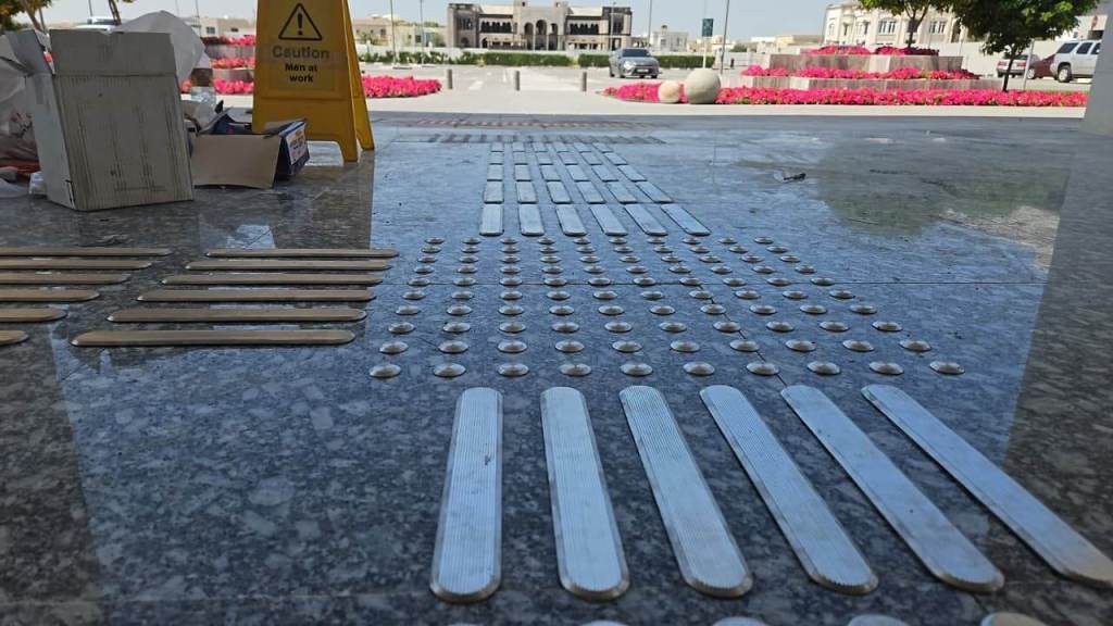 Close-up of a textured surface with tactile paving strips and warning sign, indicating ongoing construction work in a public space.