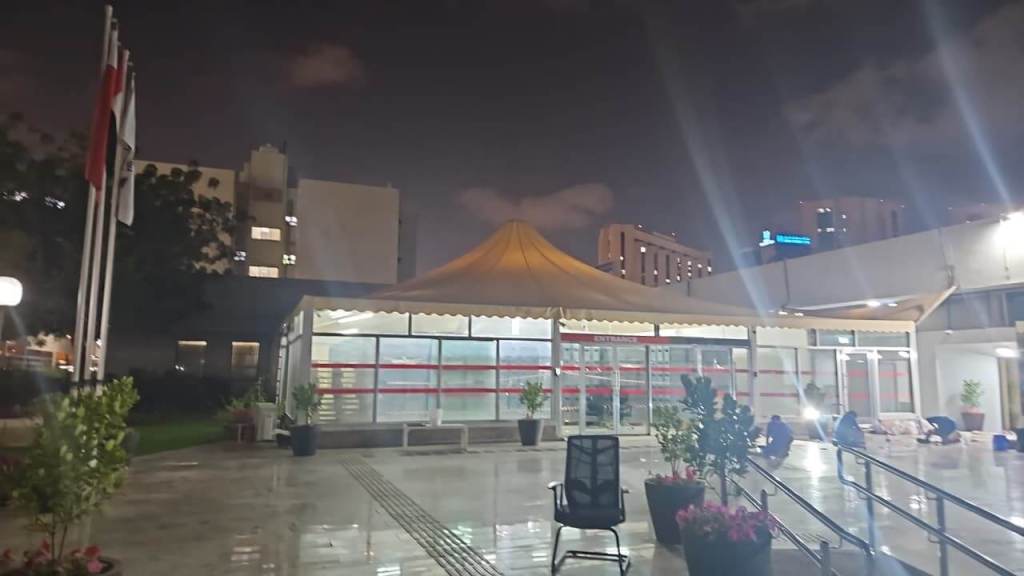 Night view of a building with a tent structure, surrounded by greenery and plants, and illuminated by lights.