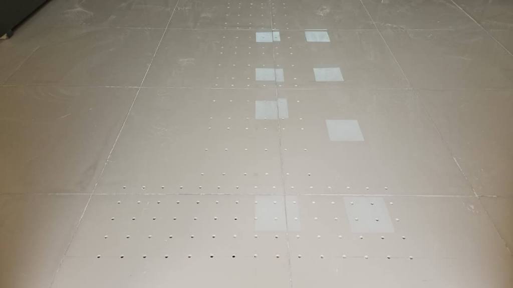 A close-up view of a polished floor featuring rectangular sections and a series of small holes, creating a pattern across the surface.