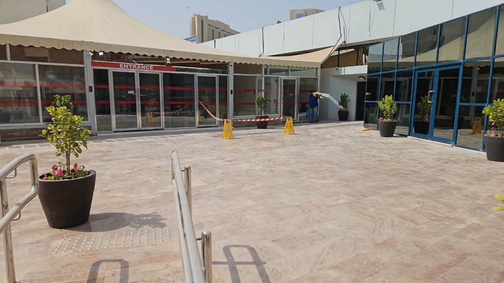 Entrance area with automatic glass doors, safety cones, and decorative planters in a plaza setting.