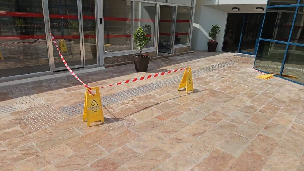 An exterior view of a building entrance with wet floor caution signs and warning tape restricting access.