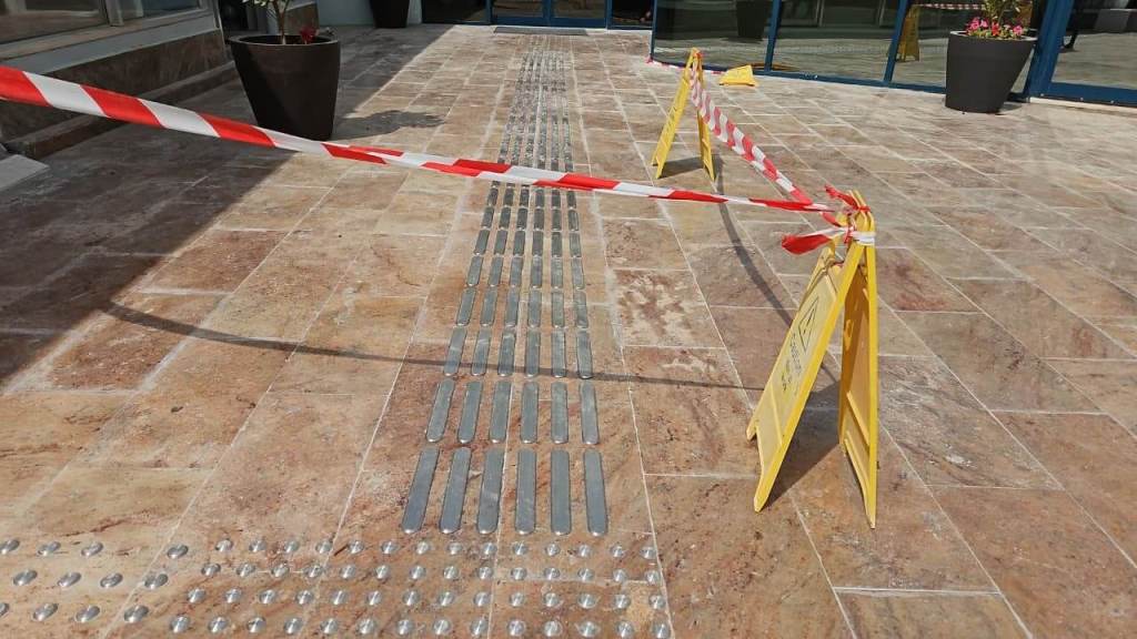 Photo of a tiled walkway with warning signs and barrier tape indicating a restricted area.