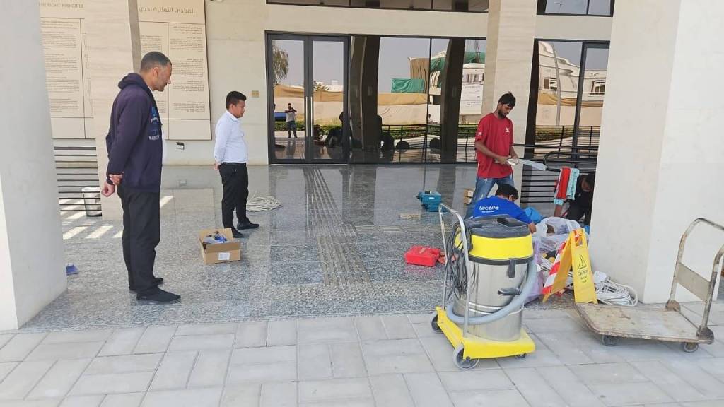 Workers cleaning the entrance of a building, with one person observing.