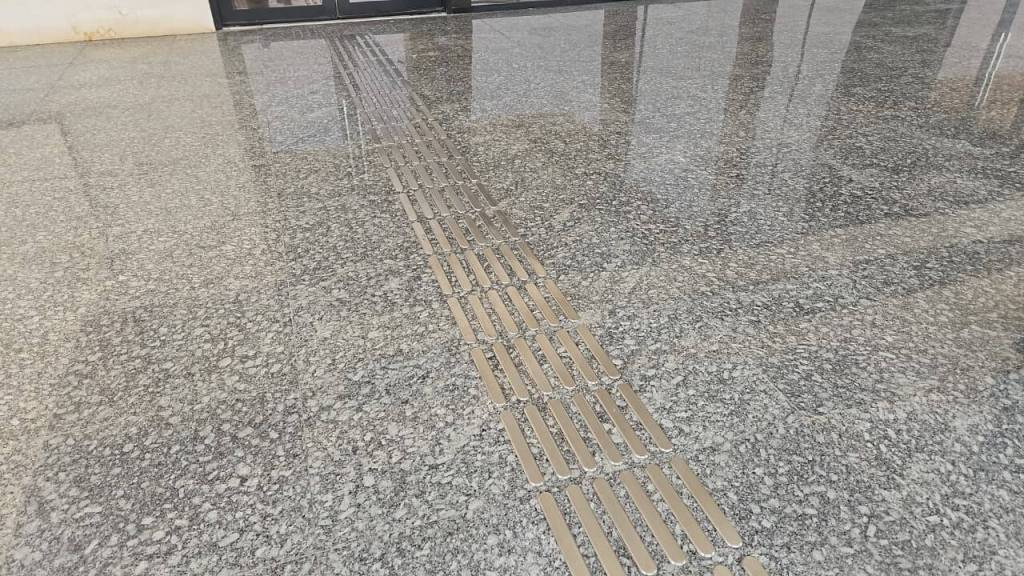 Close-up of a polished granite floor with a metallic tactile guide strip in the center.